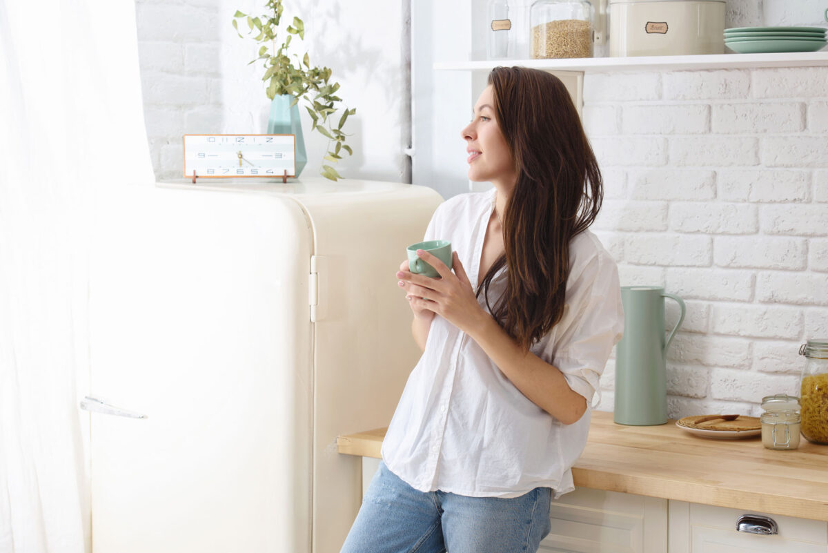 Woman holding mug leaning on kitchen bench
