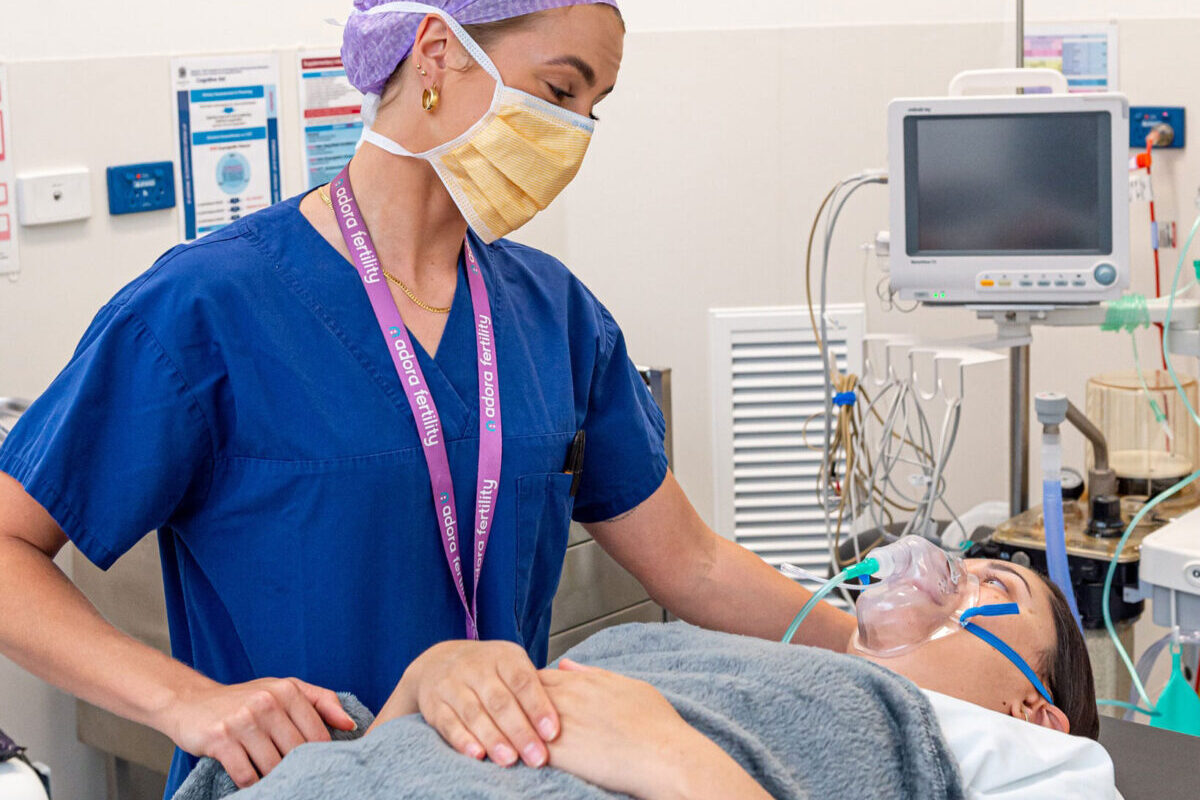 Nurse with woman lying on hospital bed for egg retrieval procedure