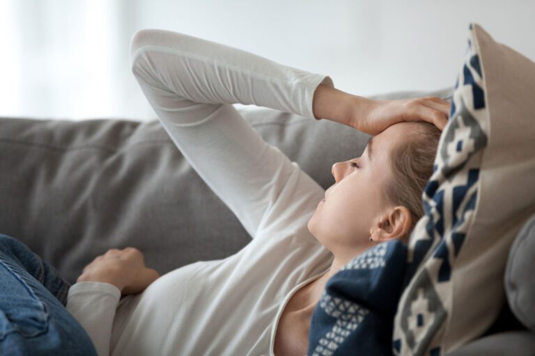 Two week wait pregnancy symptoms: A woman lies on a couch, appearing to feel unwell or anxious